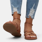 Brown sandals worn with ripped jeans on a white background
